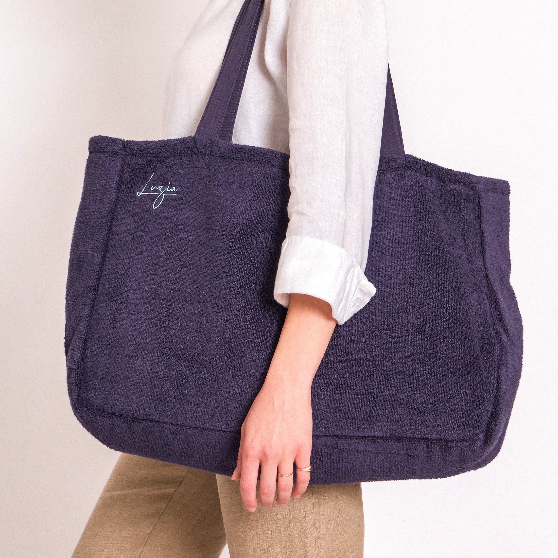 Person holding a Navy blue tote bag with 'Luzia' branding on a plain background